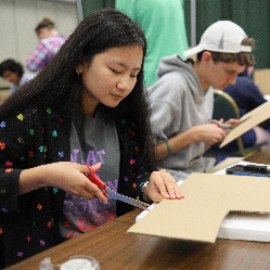 A student in NFB EQ cutting cardboard with a pair of scissors.