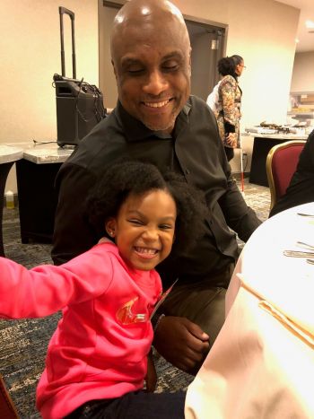Shawn Callaway and his daughter sit at a table both with big happy smiles.