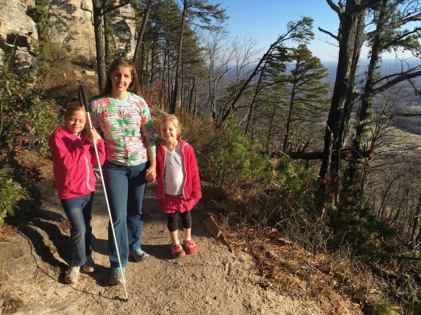 A blind Mom poses with her two daughters for a picture on a hiking trail.