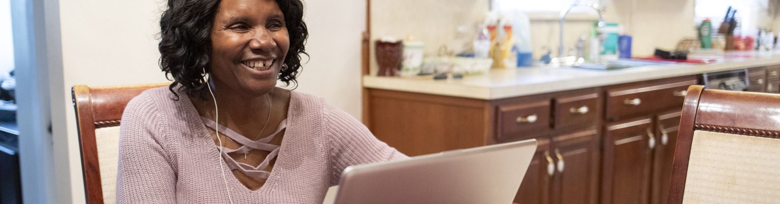 A blind woman smiles while using her laptop at dining room table