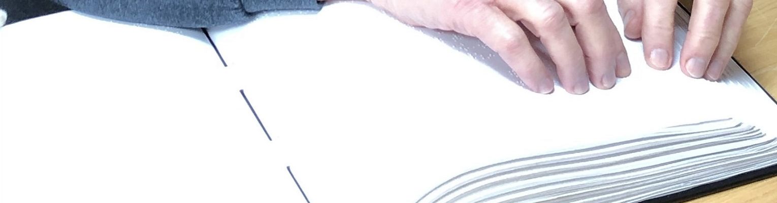 A man's fingertips read a Braille book.