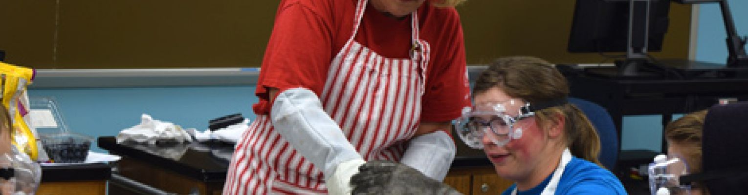 Mary Ann and a student stand over a boiling pot wearing goggles.