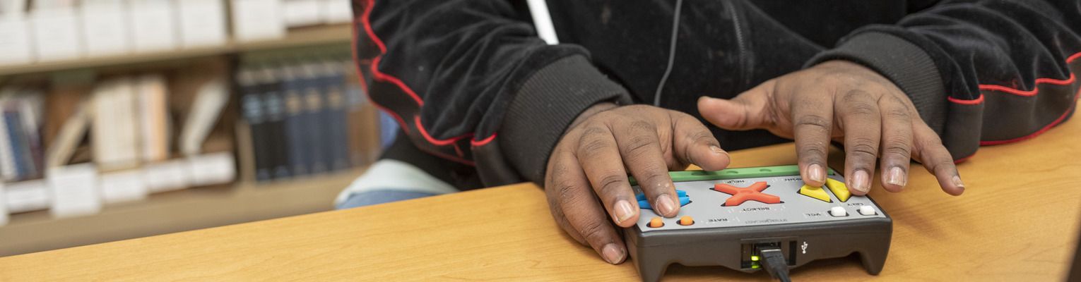 A close up of hands using the tactile key pad of an accessible voting machine.