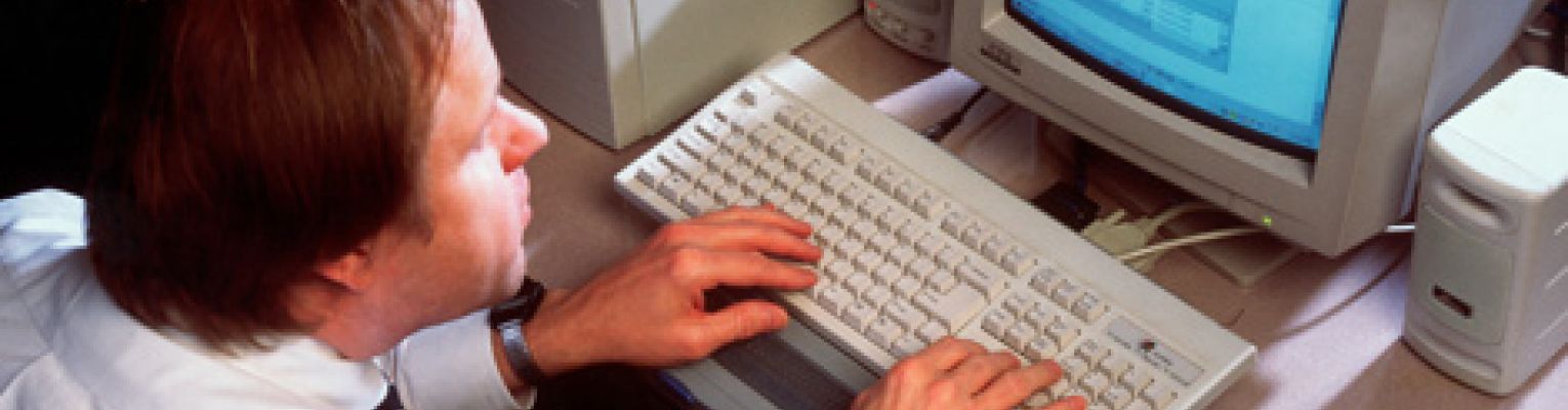 A blind man sits and works at a computer.